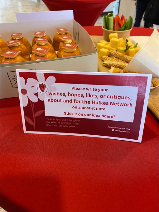 The picture shows cakes with the Halkes logo, a snack platter, and a sign which says "please write your wishes, hopes, or critiques, about and for the Halkes Network on a note. Stick it on our idea board." 
