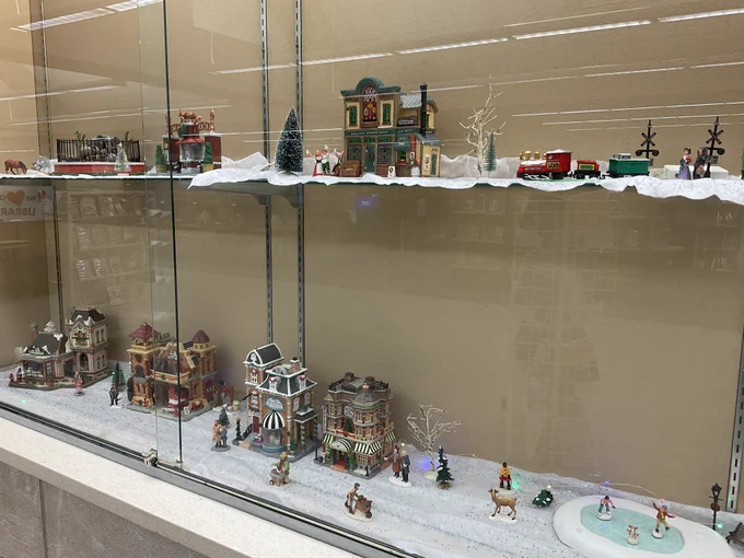 A glass display case lined with white felt on the bottom for snow and filled with ceramic figurines and buildings that light up