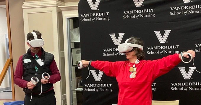 Woman in red sweater and virtual reality headset motions while a man in a headset stands by
