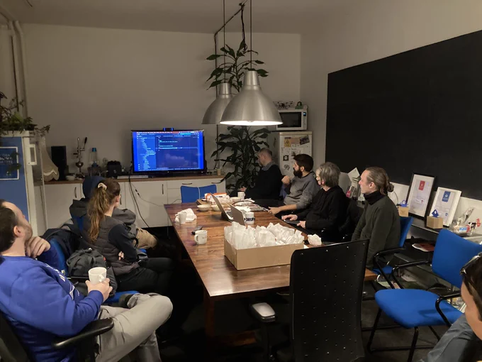 people on chairs around a conference table looking at a screen