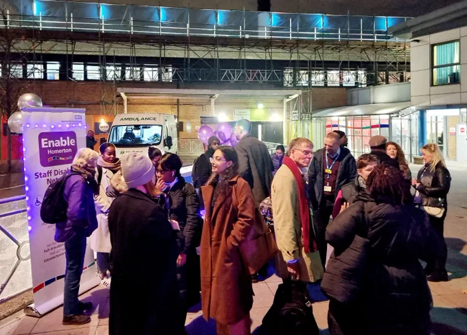 Crowd of people outside the hospital with purple balloons, purple lights and the Enable Homerton information banner