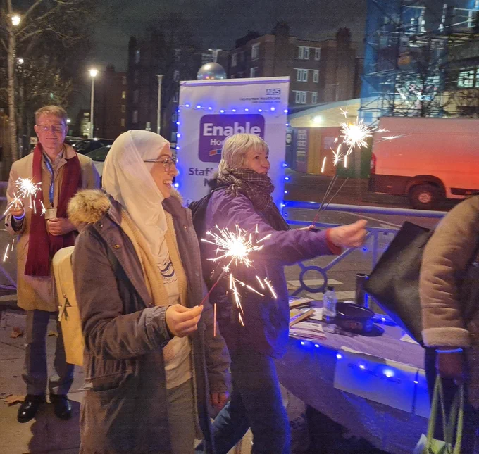 Three smiling people with sparklers and the Enable information banner and purple lights behind them