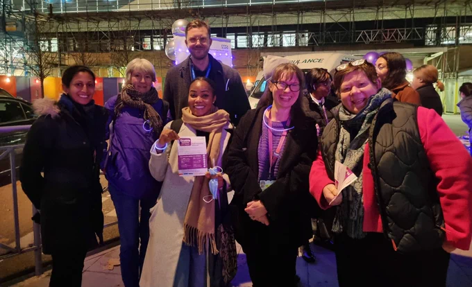 6 smiling people, including the Director of People and the CEO, outside the hospital wearing purple glow sticks.