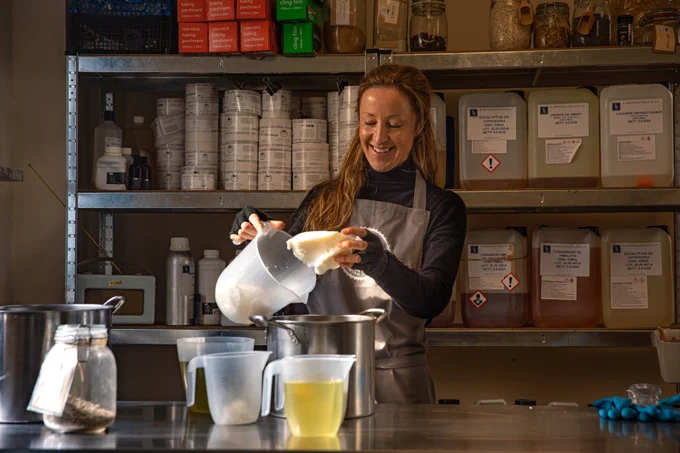 Dartmoor Soap company. Lady pouring ingredients to make soap with industrial shelves holding ither ingredients behind her.