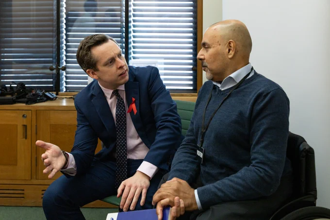 This is an image of Minister for Disabled People, Tom Pursglove in a navy suit, pink shirt and patterned tie sitting beside Kamran Malik. They are engaged in conversation.  