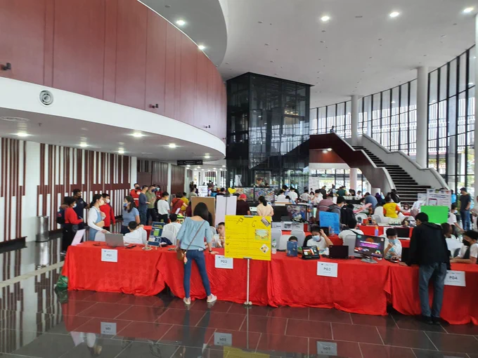 View from the entrance of the hall with serried ranks of projects on long red tables sporting bright red table cloths. The projects continue around the corner, people are engaging with the young makers exhibiting. 