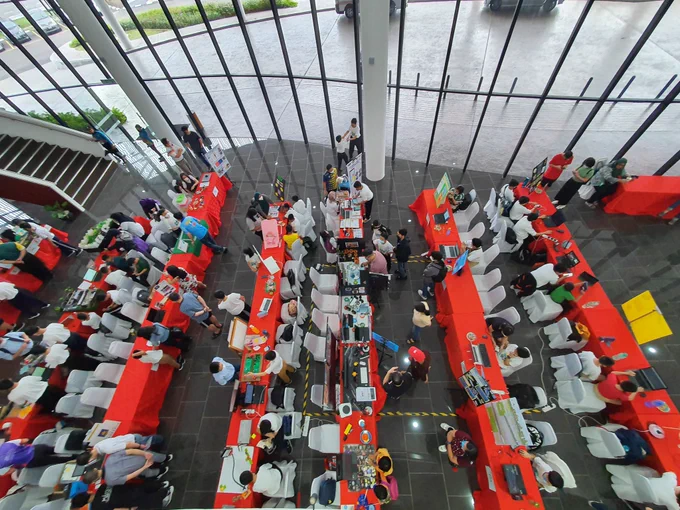 Aerial view of a hall with bright red table cloths covered in projects. There are laptops and models and kids everywhere exhibiting and browsing (some adults too) 
