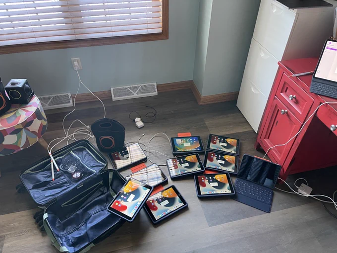 10 iPads open on the floor, charging with an airdrop popup on their screens. On the side, there is a skoog (adaptive musical instrument). 
