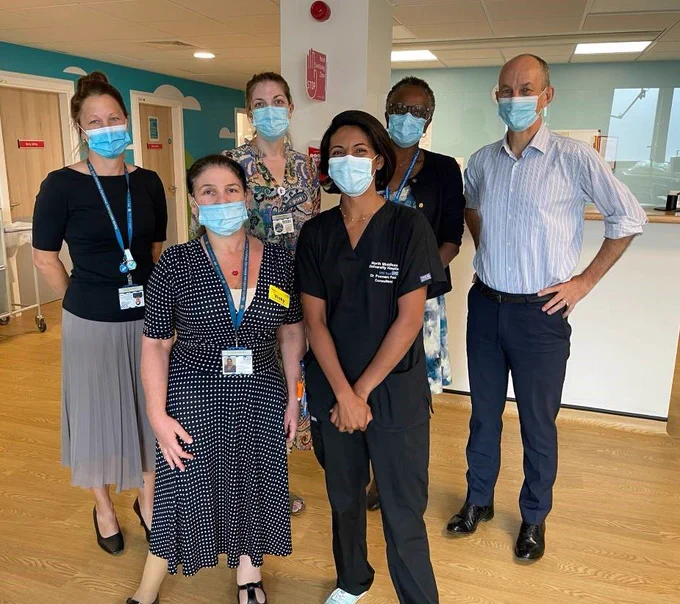 Vicky stands at the front of her team of 6. Everyone is wearing work clothes and wearing a mask.