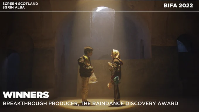 Two children in Aran look at each other in stone room. A spotlight from above shines down them. Text reads "Winners. BREAKTHROUGH PRODUCER
THE RAINDANCE DISCOVERY AWARD"