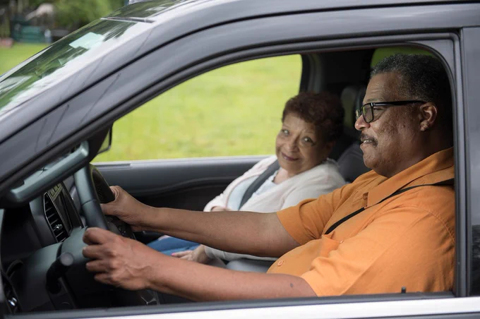 Older man driving a vehicle with an older woman in the passenger seat