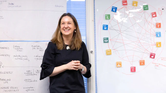 Caroline Howe standing in front of whiteboards with diagrams on them