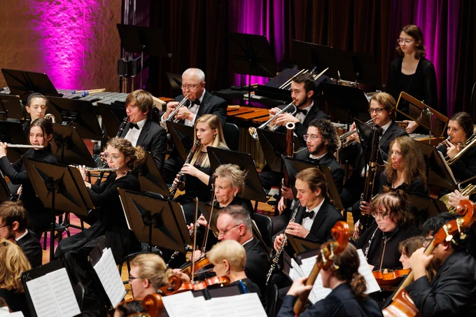 Members of the University and Community Orchestra perform on stage during Purdue Fort Wayne's Home for the Holidays concert. The image includes brass, woodwind, and string instrumentalists.
