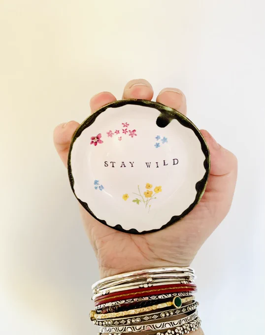 Hand gripping a small trinket dish decorated with the words ‘stay wild’ and paintings of flowers