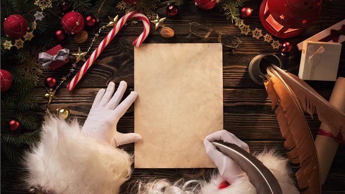 Santa holding a quill about to write on a piece of paper.