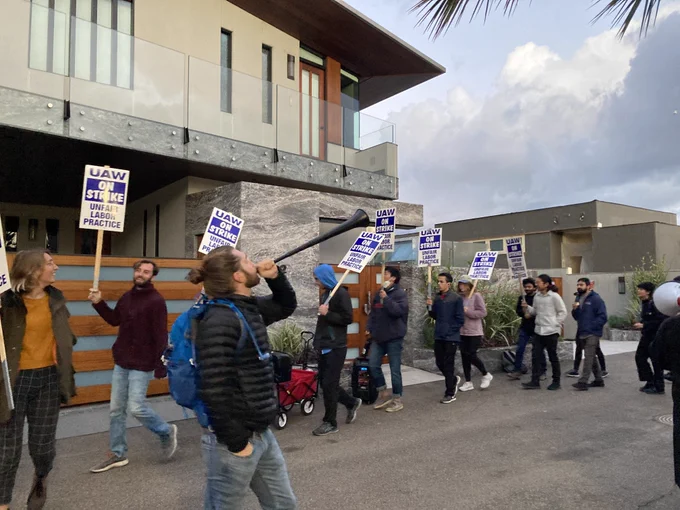 A crowd of workers holding 'UAW on strike' signs protesting outside of the modern beachfront home of UC San Diego donor Gary Jacobs.