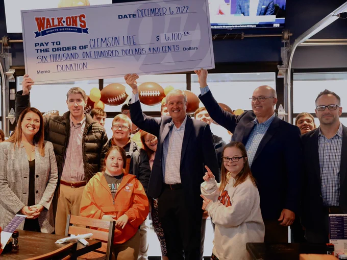 Large check to ClemsonLIFE held in the air with a large group smiling at Walk-Ons