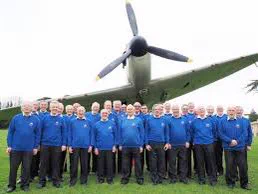 A Mass of about 40 men in blue jumpers stood in front of an old spitfire.