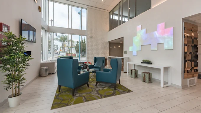 Lexen Hotel North Hollywood lobby with blue arm chairs, bright green rug, flooring, plants, TV, other furniture and tech art. 