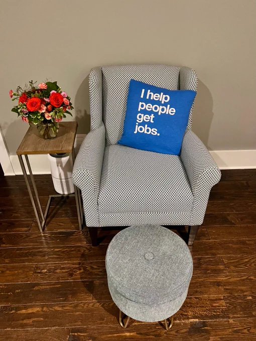 Gray chair holding blue pillow that says "I help people get jobs" 