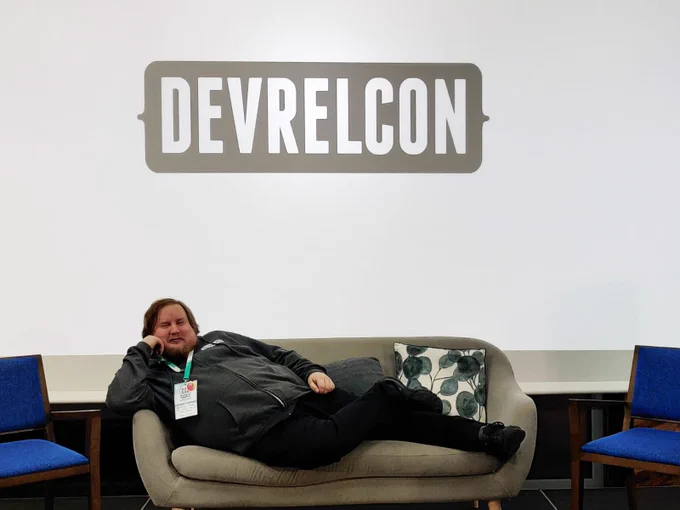 Me lying on a couch with large DevRelCon logo behind me on a projector screen