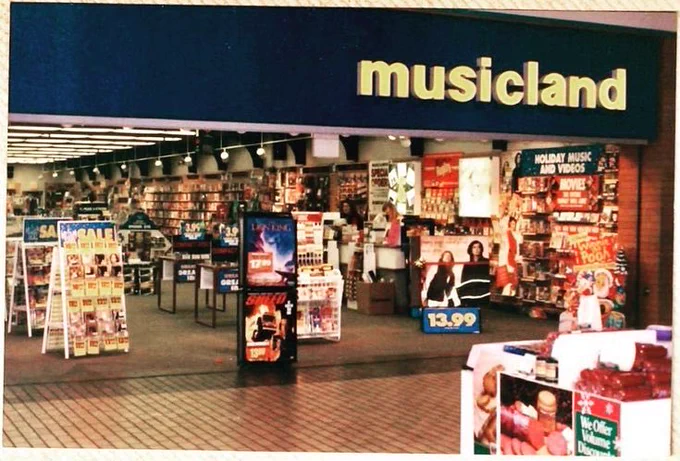 A photo of a store called "Musicland" which no longer exists. It was a store located in shopping malls and sold music in the form of vinyl records and cassette tapes. A dinosaur on every front.