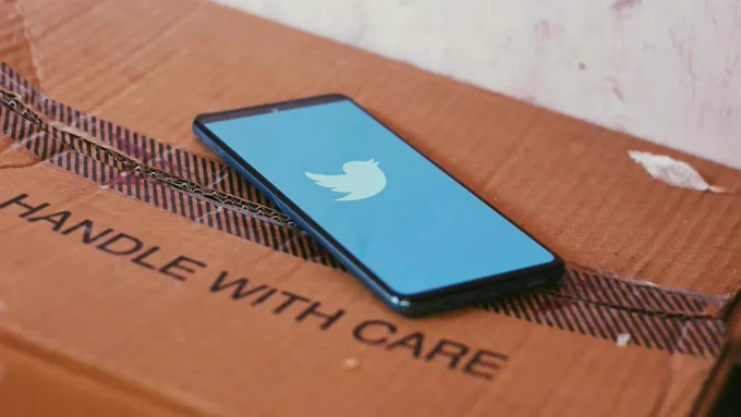 Smartphone mit auf dem Display angezeigtem Twitter-Logo liegt auf einer Kartonbox mit der Aufschrift "Handle with Care".