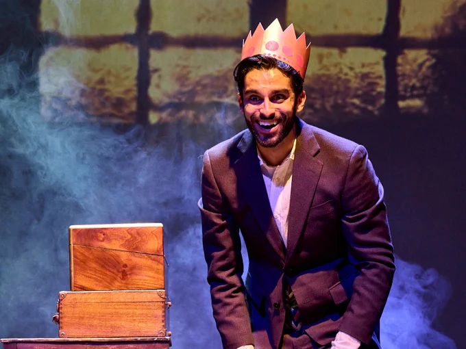 3 - Eben Figueiredo stands upon a stack of wooden chests. He has a paper Christmas hat on and is grinning with his hands on his knees.
