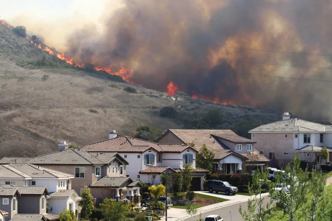 A wildfire burning with smoke filling the surrounding air behind a row of houses
