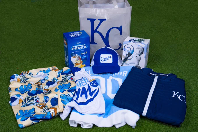 A photo of a collection of gameday giveaway items.

List of items:
Royals Hawaiian Shirt
Royals "Together Royal" Hooded T-Shirt
Royals Sluggerrr Hooded Towel
Royals Puffy Vest
Salvador Perez Bobblehead
Royals Trucker Hat
Nicky Lopez Bobblehead
Royals Tote Bag