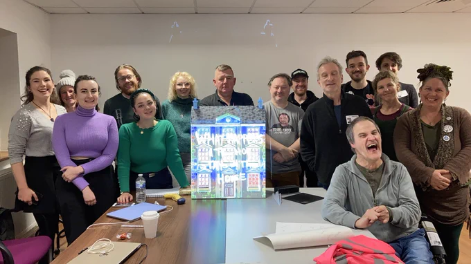 The group of smiling participants in our LEAP learning programme, gathered around a doll’s house onto which a projected image is being thrown, created over the course of the workshop.