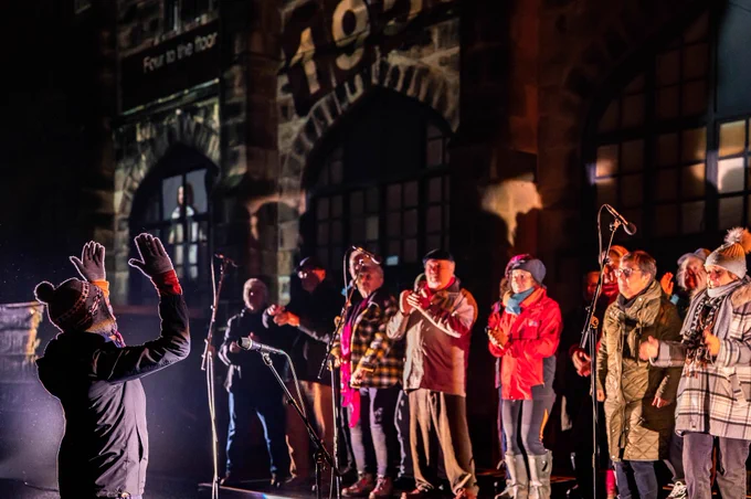 📷by Robin Zahler. Photo taken during a performance of 100 Stories High, James Hamilton in front of a choir of singers dressed in warm winter hats & coats!