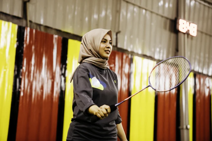Woman holding a badminton racquet inside a sports hall.