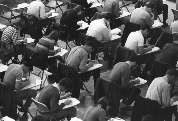 Waterloo Lutheran University students writing exams in May 1969. They are seated in rows and each student is sitting in a chair with an attached writing arm.