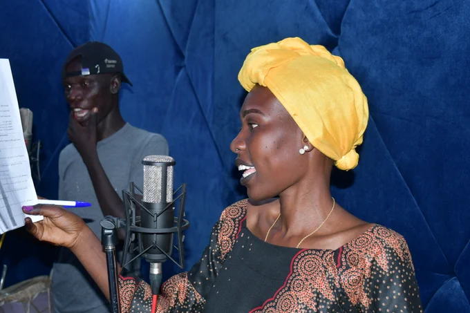 a woman with a yellow headscarf tied up speaks into a microphone