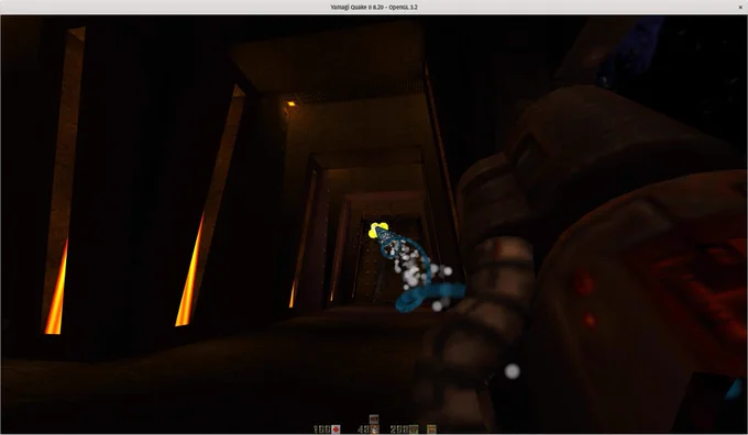 A screenshot of the first person shooter Quake 2, running in the Yamagi Quake 2 source port.
There's a dark corridor with some long vertical lights in the walls and the railgun is being shot, it shoots a spiralling blue particle beam (with white particles in the center), at the end there's an explosion, where a flying enemy was hit.
