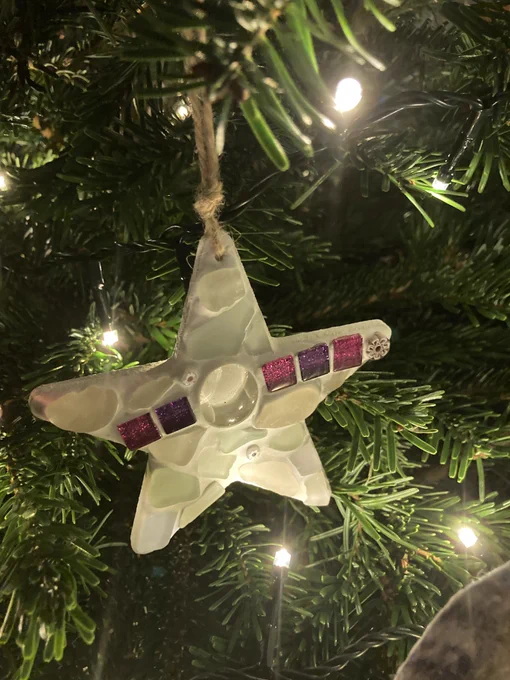 A star made from seaglass hanging on a real Christmas tree, surrounded by white twinkling lights.