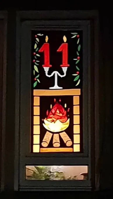 Festive window display to mark the 11th day of advent with a log fire and two candles in the shape of the number 11.