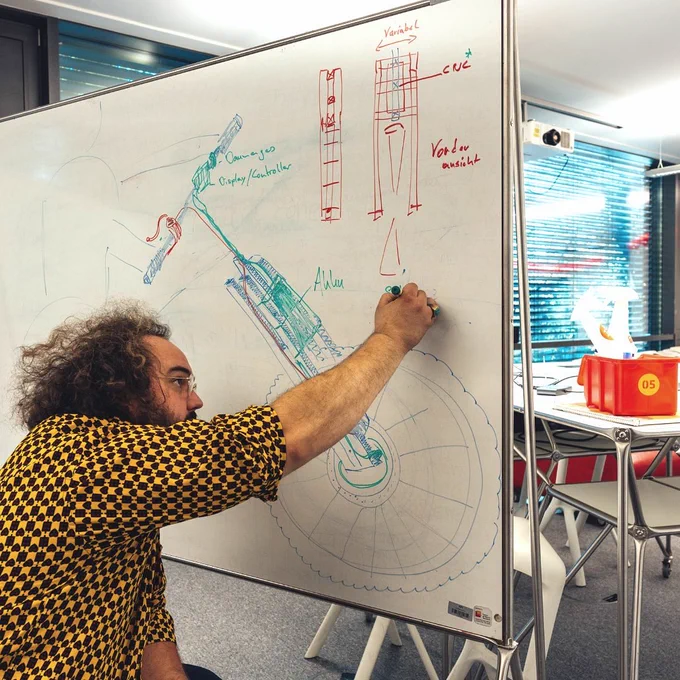 Eine Person zeichnet auf einem Whiteboard ein Vorsatzrad für einen Rollstuhl.