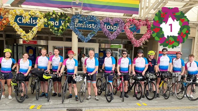 10 cyclists standing in a row with their bikes outside the main entrance of Chelsea and Westminster Hospital. The cyclists are wearing CW  branded cycling clothing. At the top there’s a graphic of a wreath with the number one inside it. 