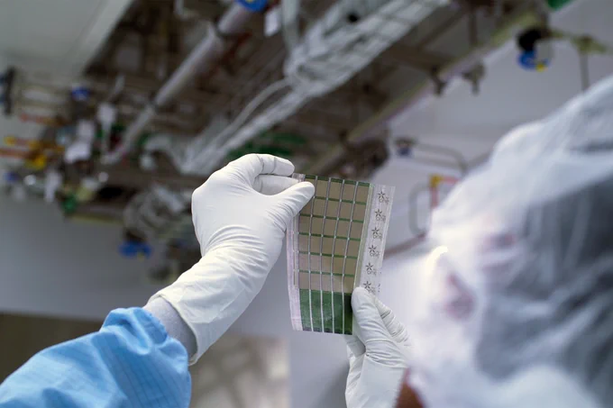 Someone wearing latex gloves holding up a sheet containing 6x5 grid of solar cells toward a light.