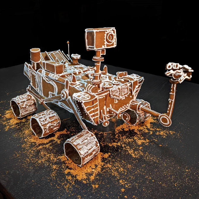 A 3D model of the Mars Curiosity Rover with many details in icing. It sits atop reddish gingerbread "dirt".