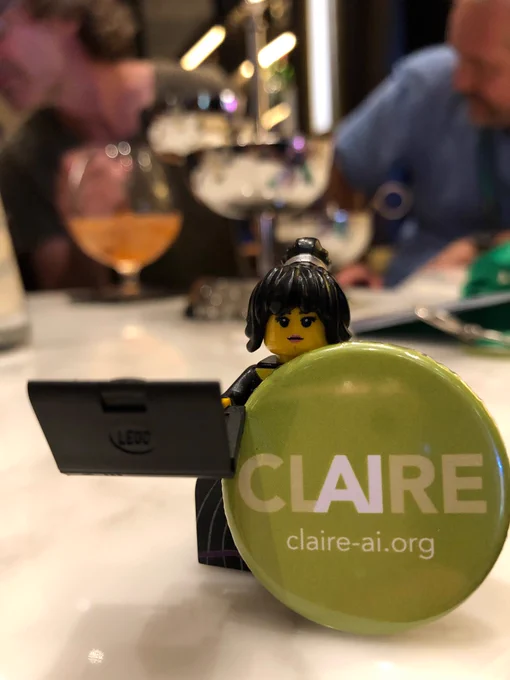 Little Lego figure with black hair, holding a laptop and a green button that has “CL AI RE Claire-ai.org” written on it.