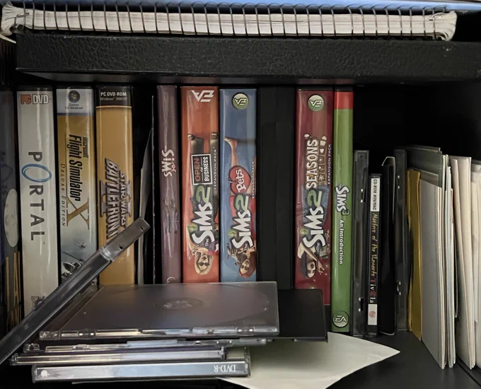 a cabinet full of computer game CD boxes from the early 2000s: portal, flight simulator X, Star Wars battlefront (2005), the sims, the sims 2 open for business, the sims 2 pets, the sims 2 seasons, the sims 3: an introduction