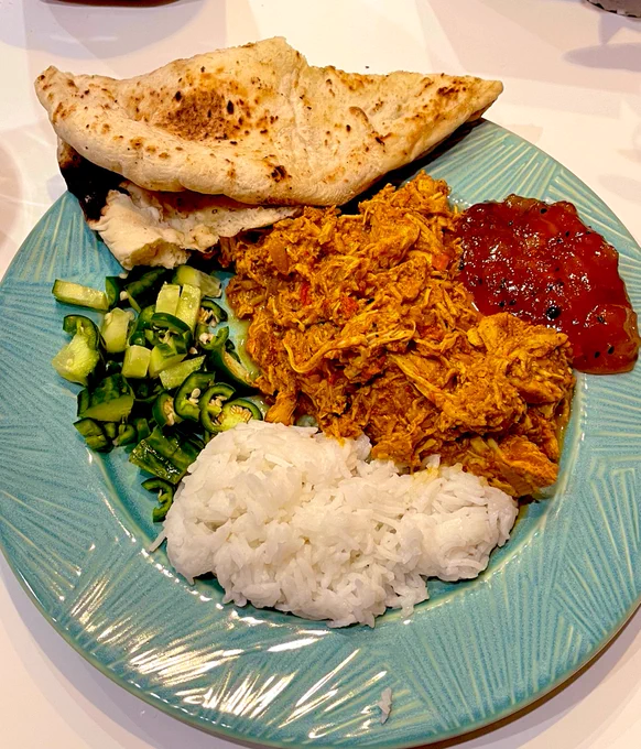 A plate of Turkey curry, rice, chilli and cucumber salad and naan.