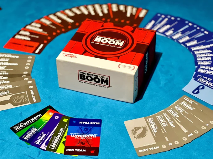 A selection of the character cards are assembled in a circle around the game box. The blue team cards, the red team cards, the grey team cards are grouped together. Some wild cards are places at the bottom of the circle