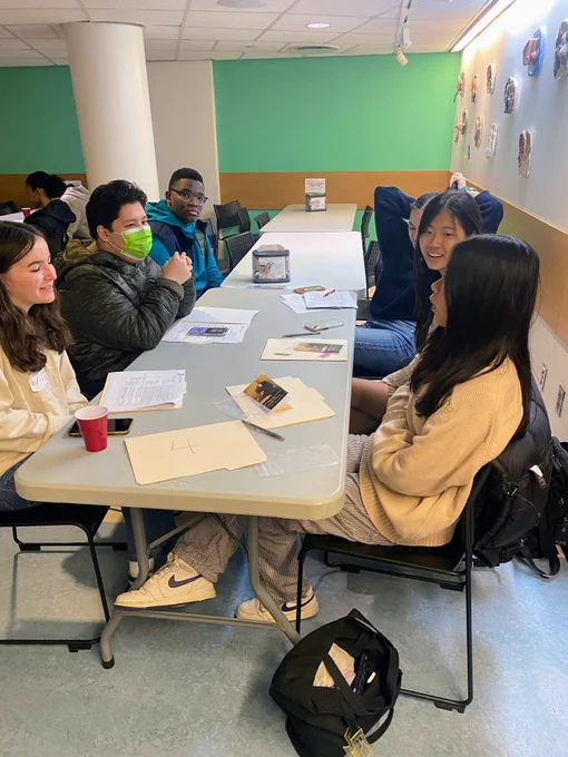 A group of high school students sitting around a folding table and participating in a discussion.