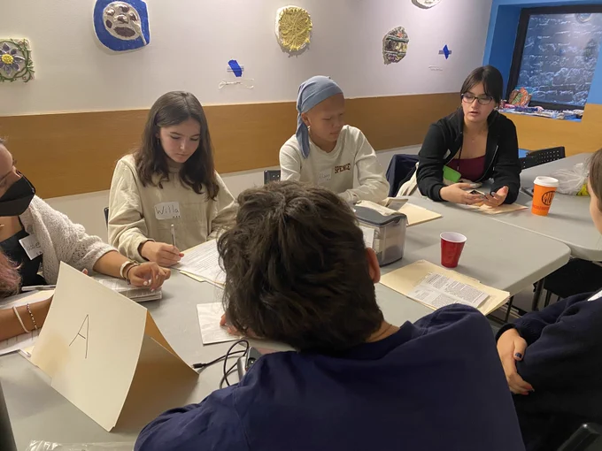 A group of high school students sitting around a folding table and participating in a discussion.