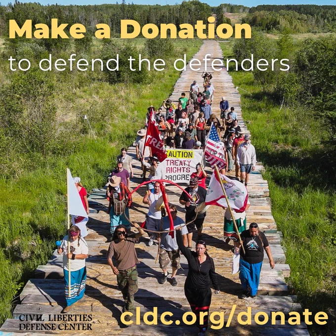 A wooden walkway crosses through lush green marshland along the banks of the Mississippi River. Indigenous Water Protectors and their treaty allies walk with signs, flags, and banners to engage in ceremony on their sacred lands which are threatened by Enbridge's Line 3 oil pipeline. Text reads: Make a donation to defend the defenders. CLDC.ORG/DONATE