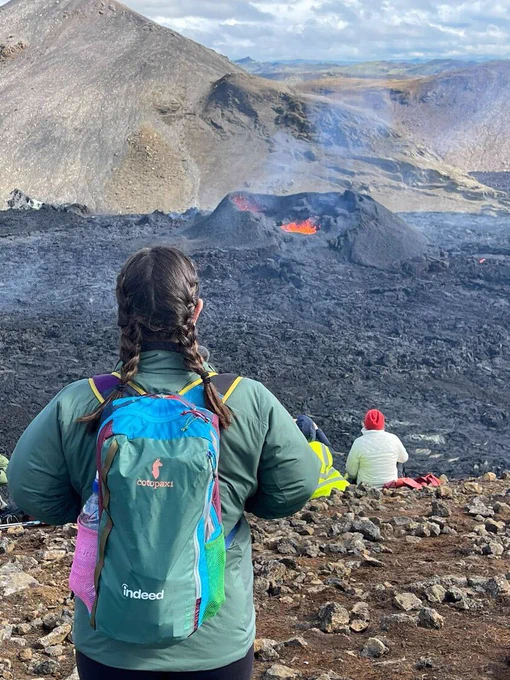 Woman wearing an Indeed backpack standing before an active volcano